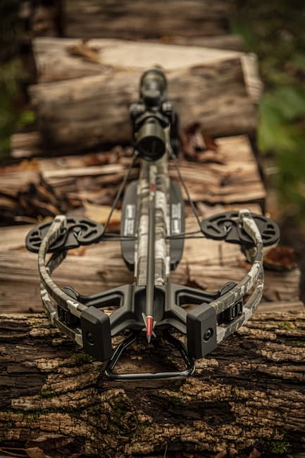 TenPoint crossbow with red tipped mechanical broadhead laying on a wood pile.