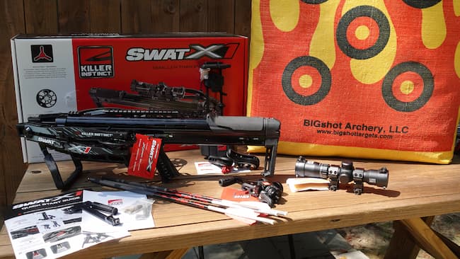 Killer Instinct SWAT crossbow on a table with arrows, scope, and block target 