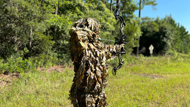 archery in camouflage holding a bow at full draw.