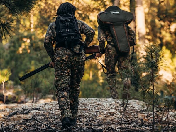 two people headed out on a hunting adventure; one carrying an air rifle, the other carrying a crossbow.